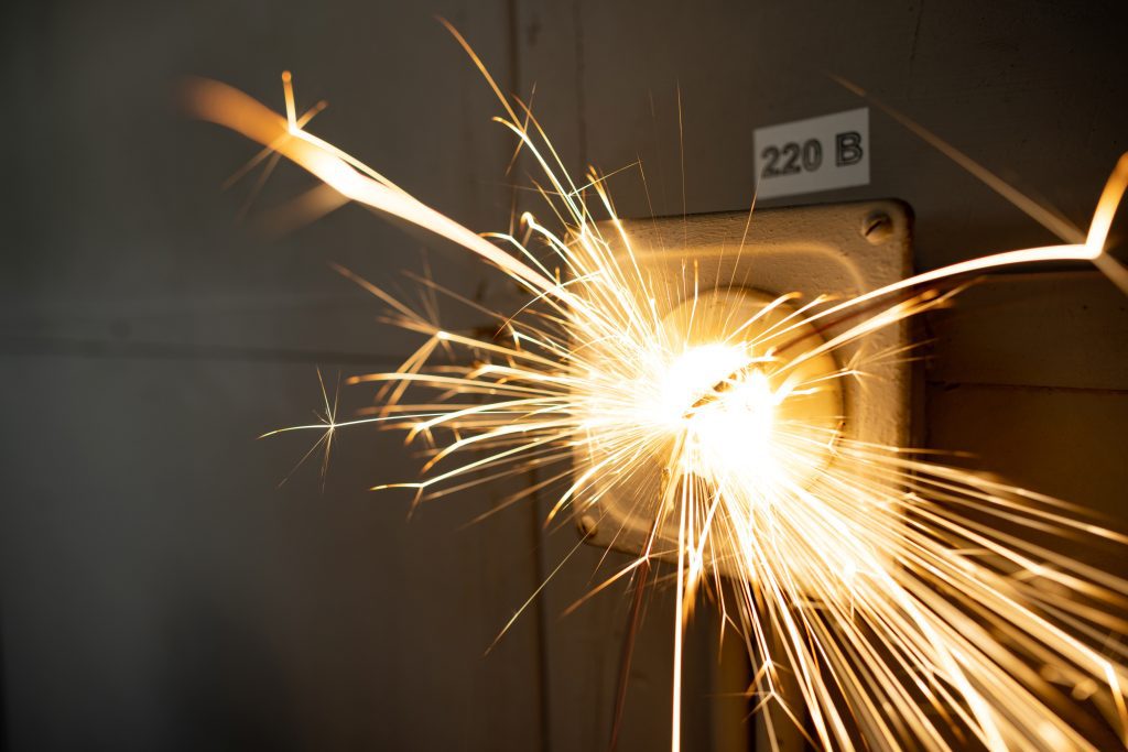 An old faulty outlet with a broken 220 volt power cord plugged in, sparkles with bright electrical dangerous sparks and produces a short circuit