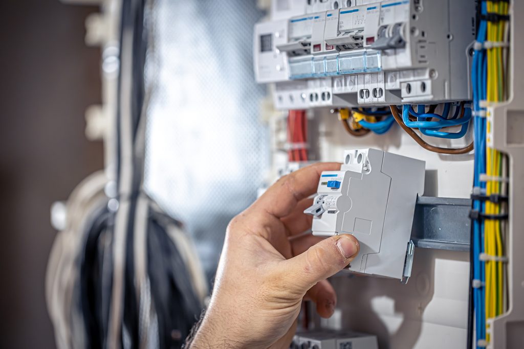 Male electrician at the checkout counter on a blurred background of a switchboard.